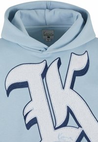 Light blue hoodie with a large, embroidered letter "K" in white and navy, featuring textured detailing. Soft fabric, adjustable hood.