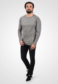 Langærmet, gråmeleret t-shirt med grå raglanærmer, parret med slim-fit sorte jeans og sorte sneakers med guldaccenter.