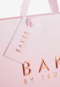 Rožinė popierinė pirkinių maišelis su šviesiai rožine raišteliu, puošiamas iškilniu metaliniu rožinio aukso tekstu "BAKER BY TED BAKER" ir atitinkamu ženklu.