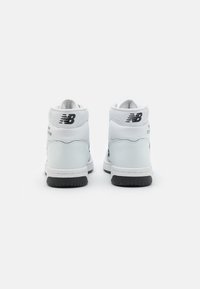 Weiße High-Top-Sneaker mit einer glatten Lederoberfläche, schwarzen Logoakzenten und einer strukturierten Gummisohle. Einfaches Design und gepolsterter Kragen.