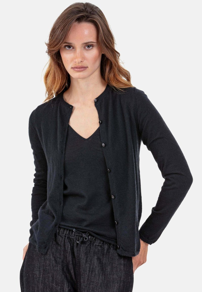 Schwarzer Cardigan aus weichem Stoff, mit rundem Ausschnitt, langen Ärmeln und Knopfverschluss. Wird über einem schwarzen V-Ausschnitt-Shirt getragen.