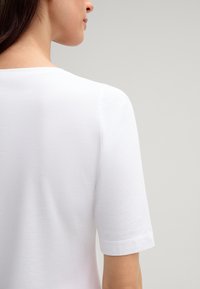 Weißes Baumwoll-T-Shirt mit rundem Halsausschnitt und kurzen Ärmeln, glatte Textur, mit einem schlichten Design und ohne sichtbare Muster oder Akzente.