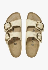 Sandali color crema con due cinturini intrecciati, ciascuno con fibbie dorate. Plantare morbido e sagomato con suola testurizzata. Numero 38 indicato all'interno.