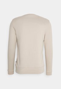 Sudadera de manga larga beige hecha de una mezcla de algodón, con un cuello redondo, puños acanalados y un dobladillo con una ligera curva en la parte posterior.
