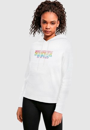 Weißer Hoodie mit dem Schriftzug "Stranger Things" in buntem, pixelartigem Schriftzug. Verfügt über eine Vordertasche und eine Kapuze mit Zugband. Glatte Stofftextur.