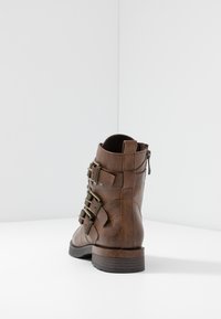 Stivaletto in pelle marrone con fibbie decorative, chiusura a cerniera e finitura testurizzata. Suola in gomma nera robusta, design strutturato.