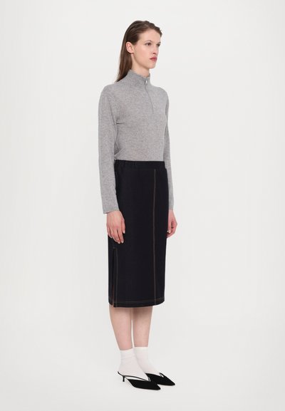 Szürke zipzáras pulóver, térdhez érő fekete szoknya narancssárga varrással, fehér zoknik és fekete hegyes orrú magassarkúk. Az összhatás sima textúrájú.