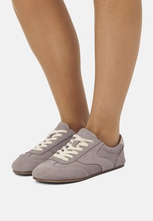 Zapatillas de gamuza moradas con cordones blancos, con un diseño bajo y punta redondeada. Incluye acentos de color claro en el talón.
