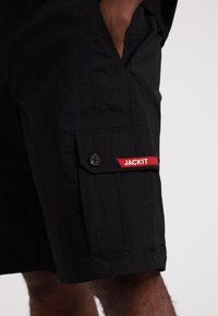 Schwarze Cargo-Shorts aus leichtem Stoff, mit Seitentaschen, Knopfverschluss und einem roten "JACK1T"-Label an der Seitentasche.