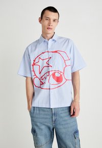 Chemise à manches courtes avec un motif rayé bleu et blanc, ornée d'un grand graphique rouge représentant une étoile et un visage de style cartoon sur le devant.