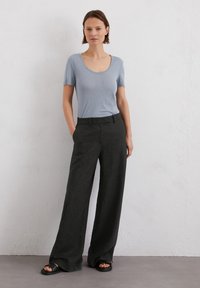 T-shirt azzurro con scollo a giro abbinato a pantaloni neri a gamba larga. Sandali con un leggero plateau. Tessuto liscio con vestibilità comoda.