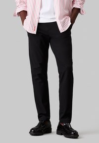 Pantalones ajustados negros, fabricados con una tela suave. Presenta un diseño clásico con una silueta limpia y un minimalismo en los detalles.