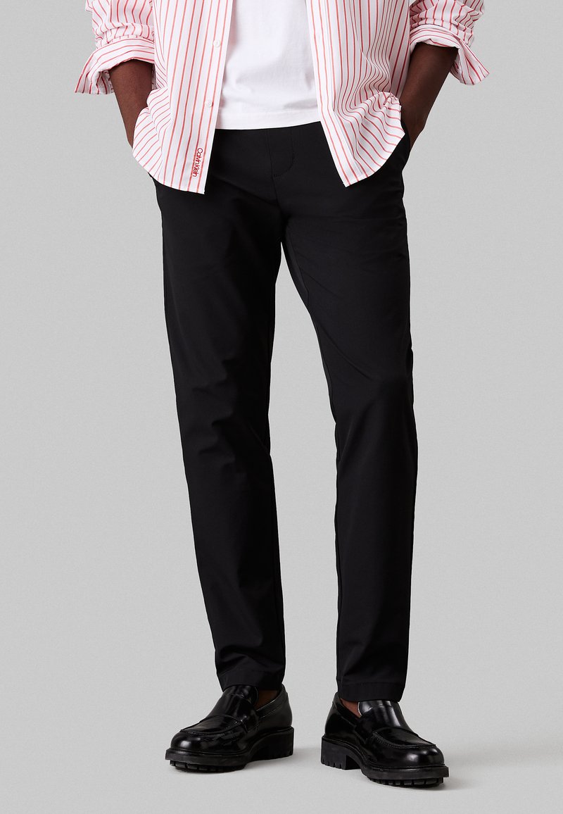 Pantalones ajustados negros, fabricados con una tela suave. Presenta un diseño clásico con una silueta limpia y un minimalismo en los detalles.