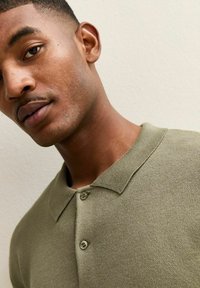 Kurzärmeliges olivgrünes Poloshirt aus strukturiertem Stoff, mit Knopfleiste und geripptem Kragen; verfügt über eine glatte Oberfläche und ein lässiges Design.