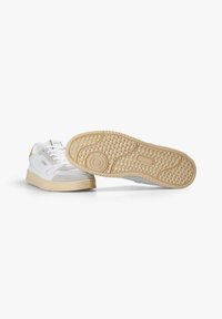 Zapatillas blancas con parte superior de ante y cuero, que cuentan con una suela de goma texturizada. El diseño incluye un acabado suave y acentos de marca mínimos.
