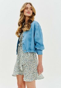 Světlemodrá zkrácená bunda s květinovou výšivkou, nošená přes smetanové šaty s modrými květinovými vzory. Oba kousky mají uvolněný střih.