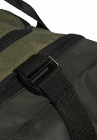 Kamuflage rygsæk med detaljer i holdbart grønt stof, sort lynlås og plastikspænde. Tekstureret overflade med kontraststing.