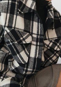 Camisa de franela de cuadros en blanco y negro, de corte grande y con un acabado texturizado, que incluye dos bolsillos en el pecho y cuello con solapa.