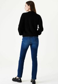 Suéter negro de canalé combinado con jeans ajustados azules y zapatos de plataforma negros. El conjunto se observa desde la parte trasera.