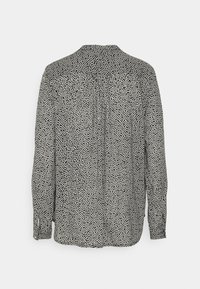 Blouse à manches longues noir et blanc avec petit motif à pois irréguliers, détail froncé sur l'empiècement dos et poignets boutonnés.