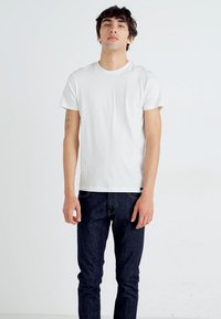 White cotton t-shirt with short sleeves, crew neckline, and a relaxed fit, paired with dark blue denim jeans. Simple design, no patterns.