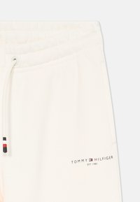 Nærbillede af cremefarvede sweatpants med elastisk liv, snor med farvede tip og Tommy Hilfiger-logo med teksten "EST. 1985".
