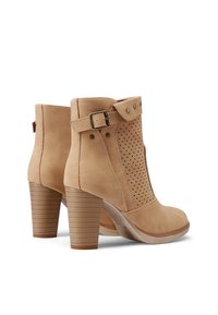 Stivali alla caviglia in pelle color cuoio con un design perforato, cinturino alla caviglia regolabile e tacco a blocco in legno. Texture liscia con punta rotonda.