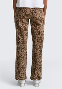 Pantalones de estampado de leopardo en tonos marrones y negros, con piernas rectas, cintura de altura media y una textura suave. Combinados con zapatillas blancas.