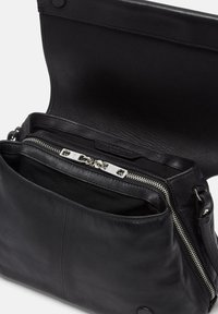 Borsa a tracolla in pelle nera con scomparto con zip e superficie liscia. Dotata di accessori in metallo argentato e design con pattina aperta. Interno foderato.