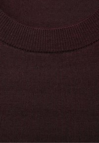 Pull en tricot côtelé bordeaux avec un col rond et un tissu texturé. Le gros plan met en valeur les coutures détaillées et les variations de couleur.