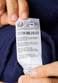 Étiquette en tissu marine avec instructions d'entretien en plusieurs langues. Matériau : 100 % coton, avec des icônes pour le lavage et le séchage.