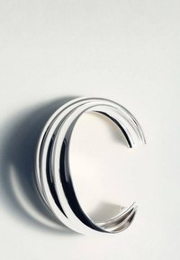Bracciale a manica in argento con tre fasce curve e lucidate, dotate di una superficie liscia e riflettente e con estremità aperte.