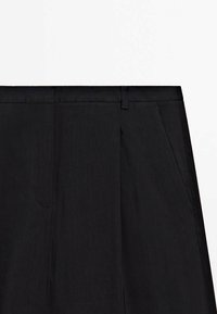 Pantaloni neri su misura con una superficie liscia, dotati di una parte anteriore piatta, due tasche laterali e passanti per la cintura. Design semplice senza decorazioni.
