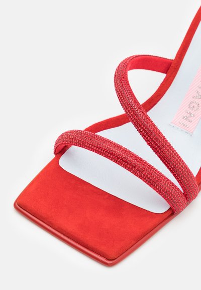 Κόκκινη ψηλοτάκουνη σανδάλι με τετράγωνη μύτη, δύο υφασμάτινες γκλίτερ ρίγες και μαλακή σουέντ υφή στην σόλα. Η εσωτερική επένδυση είναι λευκή.