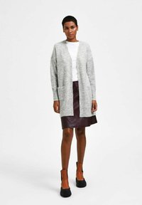 Gray knit cardigan with long sleeves and front pockets, worn over a white shirt and burgundy leather skirt, paired with brown ankle boots.