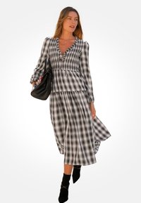 Schwarz-weißen karierten Kleid mit V-Ausschnitt, langen Ärmeln und einem ausgestellten Rock. Getragen mit einer schwarzen Handtasche und Ankle Boots.