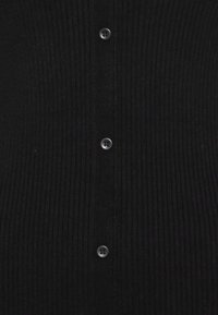 Černý žebrovaný cardigan s centrální knoflíkovou légou s tmavými knoflíky, texturovanou tkaninou a těsným střihem.