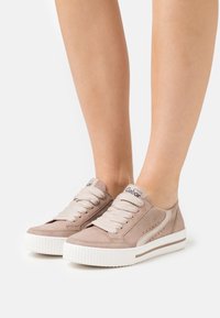 Sneaker in suede beige con suola in gomma bianca, punta rotonda e design con lacci. Presentano dettagli perforati e una targhetta con il marchio sulla linguetta.