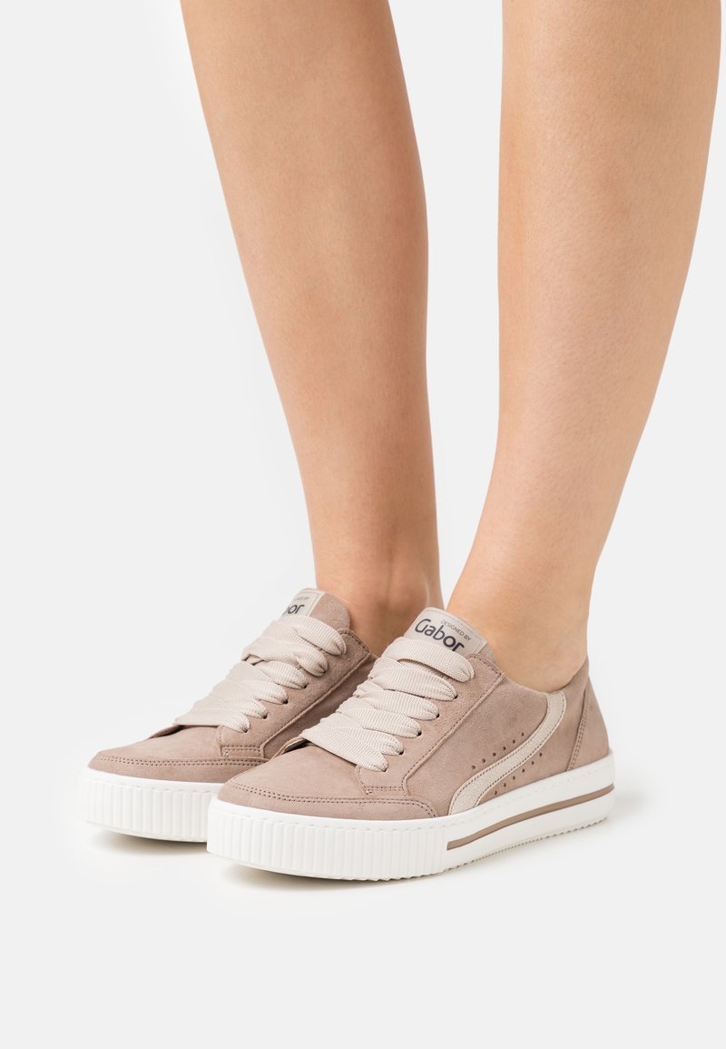 Sneaker in suede beige con suola in gomma bianca, punta rotonda e design con lacci. Presentano dettagli perforati e una targhetta con il marchio sulla linguetta.