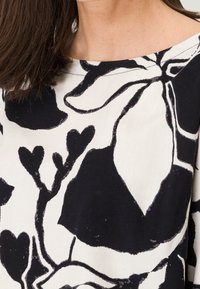 Top floral en blanco y negro con cuello redondo. La tela parece ligera y tiene una textura suave, con formas abstractas audaces.