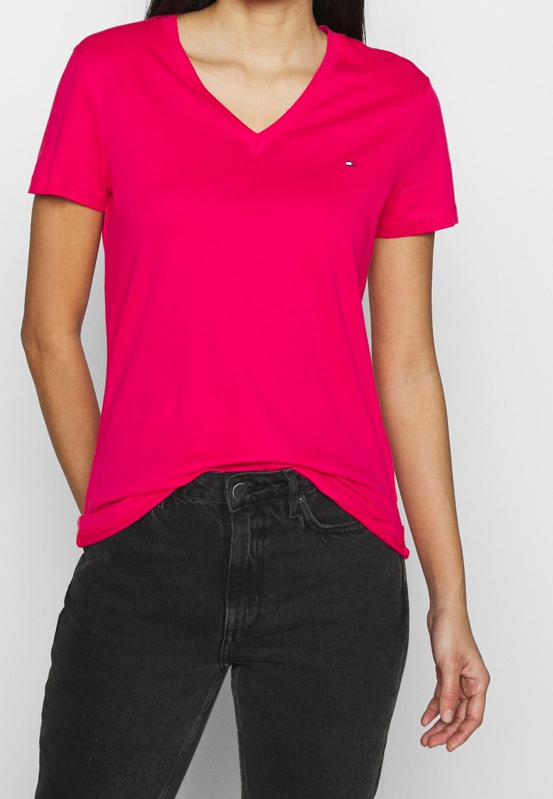 Camiseta de algodón suave de cuello en V y mangas cortas en color rosa. Presenta un logotipo sutil en el pecho y un corte holgado, combinado con jeans negros.