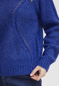 Stickad tröja i djupblått, med ett texturerat mönster och öppna maskdetaljer. Ribbad ärm- och nederkant, med en lös passform och mjuk textur.