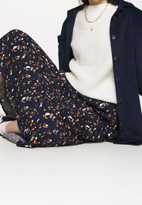 Blommig maxikjol i marinblått med mönster i orange och vitt; kombinerad med en krämfärgad tröja och en strukturerad marinblå jacka med knappar.