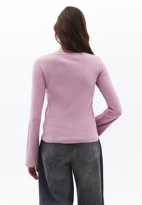 Langärmliges Oberteil aus hellrosa Stoff mit einem runden Halsausschnitt und einer figurbetonten Silhouette, kombiniert mit hoch sitzenden dunkelblauen Jeans.