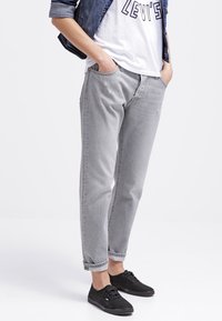 Grå denimjeans med midjehög, avslappnad passform och uppvikta benslut. Har framfickor och subtila blekningar. I kombination med svarta sneakers.