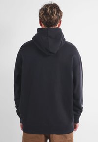 Sweat à capuche noir avec une coupe décontractée, poignets et ourlet côtelés. Texture de tissu douce et design minimaliste sans logos visibles.