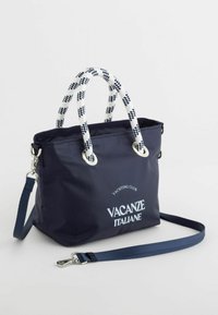 La bagagliaia in nylon blu con manici intrecciati bianchi e blu, hardware argentato e il logo stampato "VACANZE ITALIANE" sulla parte anteriore. Include una tracolla staccabile.