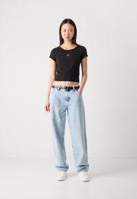 Black cropped t-shirt with short sleeves and a small logo, paired with light blue loose-fit jeans and a black belt. White sneakers.