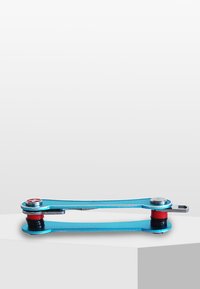 Multifunktionellt verktyg med en blå aluminiumram, två runda kontakter och röda gummidetaljer, utformat för kompakt förvaring och portabilitet.