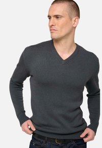 Pull en v gris à côtes avec des manches longues. Il présente une finition texturée et une silhouette ajustée, associé à un jean en denim foncé.